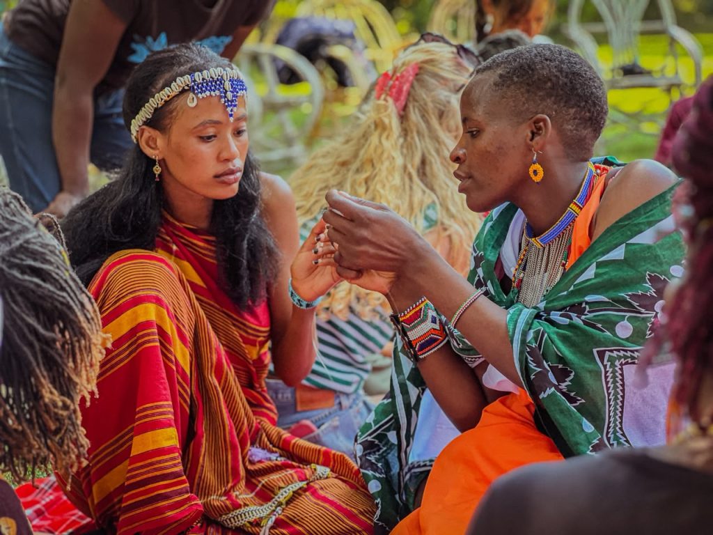 Two women in colourful Masai dresses and bead jewellery doing beadwork